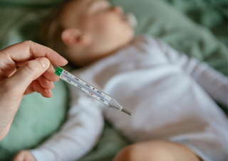 Thermometer zeigt Fieber bei schlafendem Baby, Scharlach-Behandlungstipps.