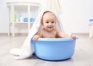 Baby in blauer Wanne mit Handtuch, lächelnd, Tipps für erstes Bad.