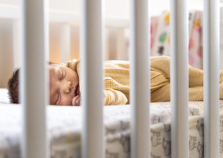 Schlafendes Baby in einem gestreiften Strampler im Gitterbett, Thema Babyablegen Tipps.