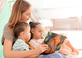 Mutter liest mit zwei Kindern ein Buch, fördert Sprachentwicklung.
