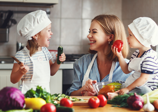 Mutter und Kinder kochen gesundes Essen in der Küche, fröhlich mit Gemüse.