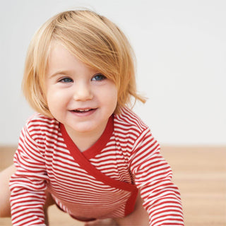 Lächelndes Kleinkind im rot-weiß gestreiften Bio-Baumwoll-Wickelbody von Living Crafts.