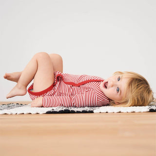 Baby in rot-weiß gestreiftem Living Crafts Wickelbody aus Bio-Baumwolle. Liegt lachend auf dem Rücken.