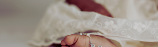 Babyfuß mit silbernem Armband und Spitze, ideales Taufgeschenk.
