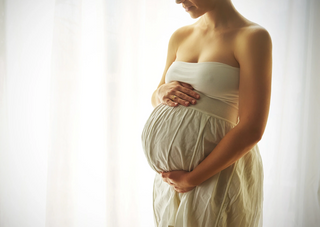 Schwangere Frau im weißen Kleid hält ihren Bauch vor hellem Hintergrund. 10 Tipps für Schwangere kurz vor der Geburt.